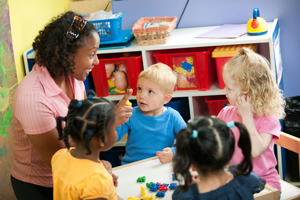 teacher surrounded by four young children in a classroom